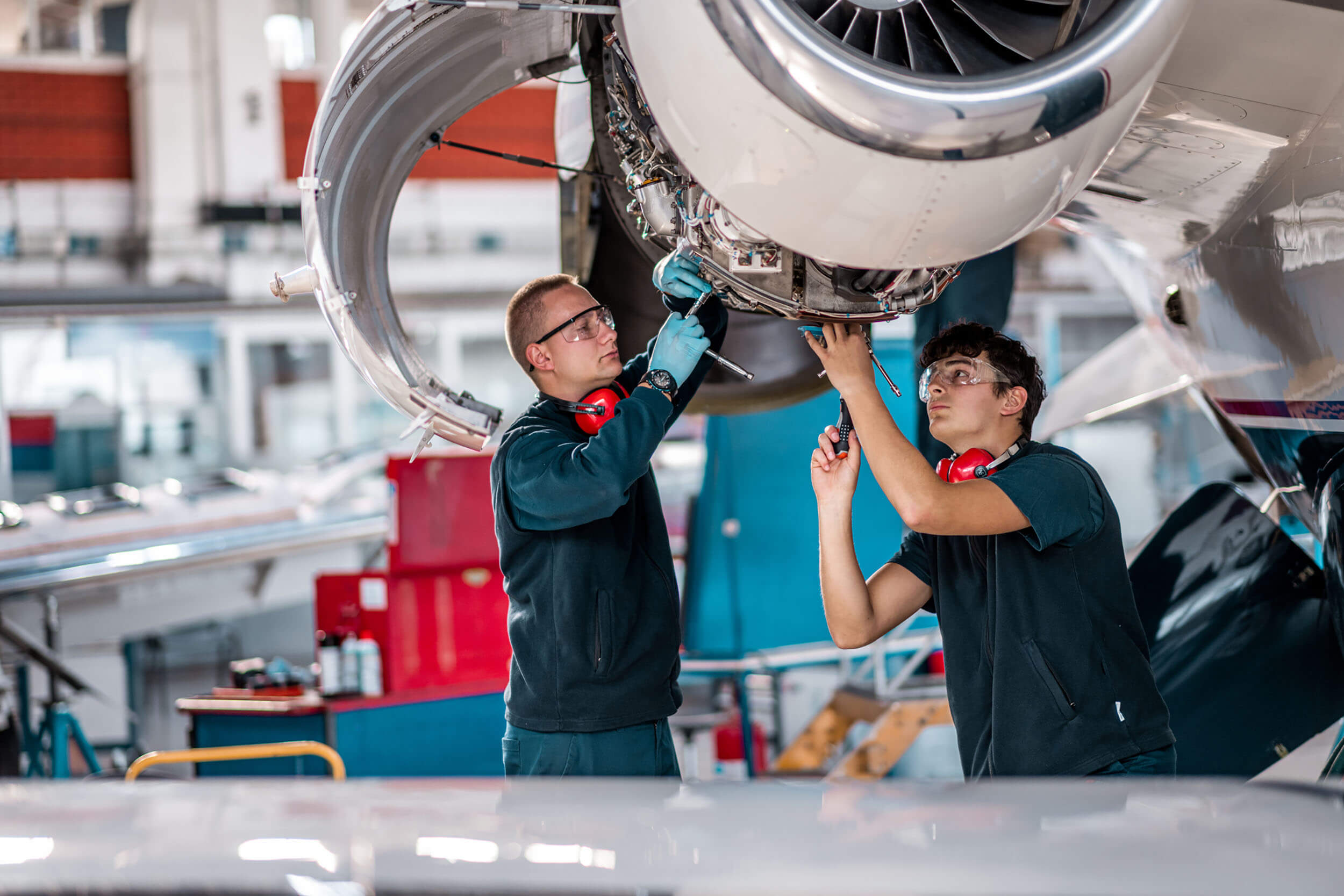 Two male aircraft maintenance mechanics inspect and check an airplane jet engine in the airport hangar.