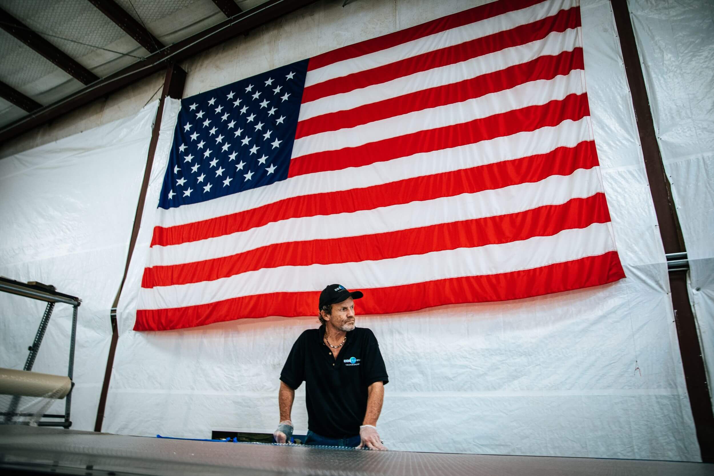 Person stands in front of hanging American flag in manufacturing facility,