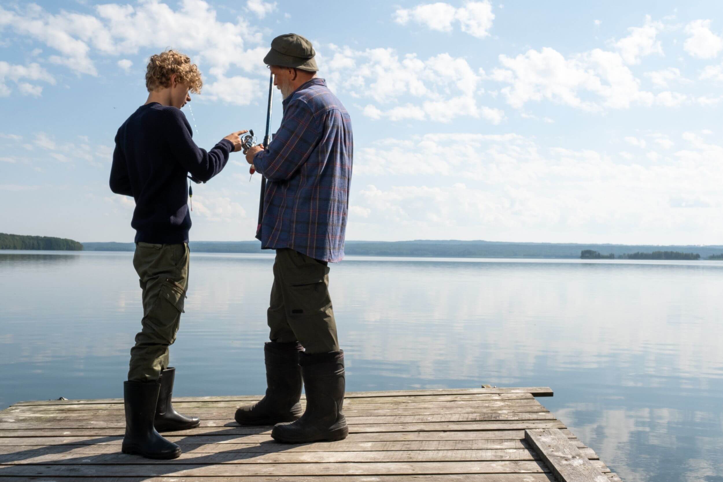 Grandfather teaches grandwon how to fish on lake.