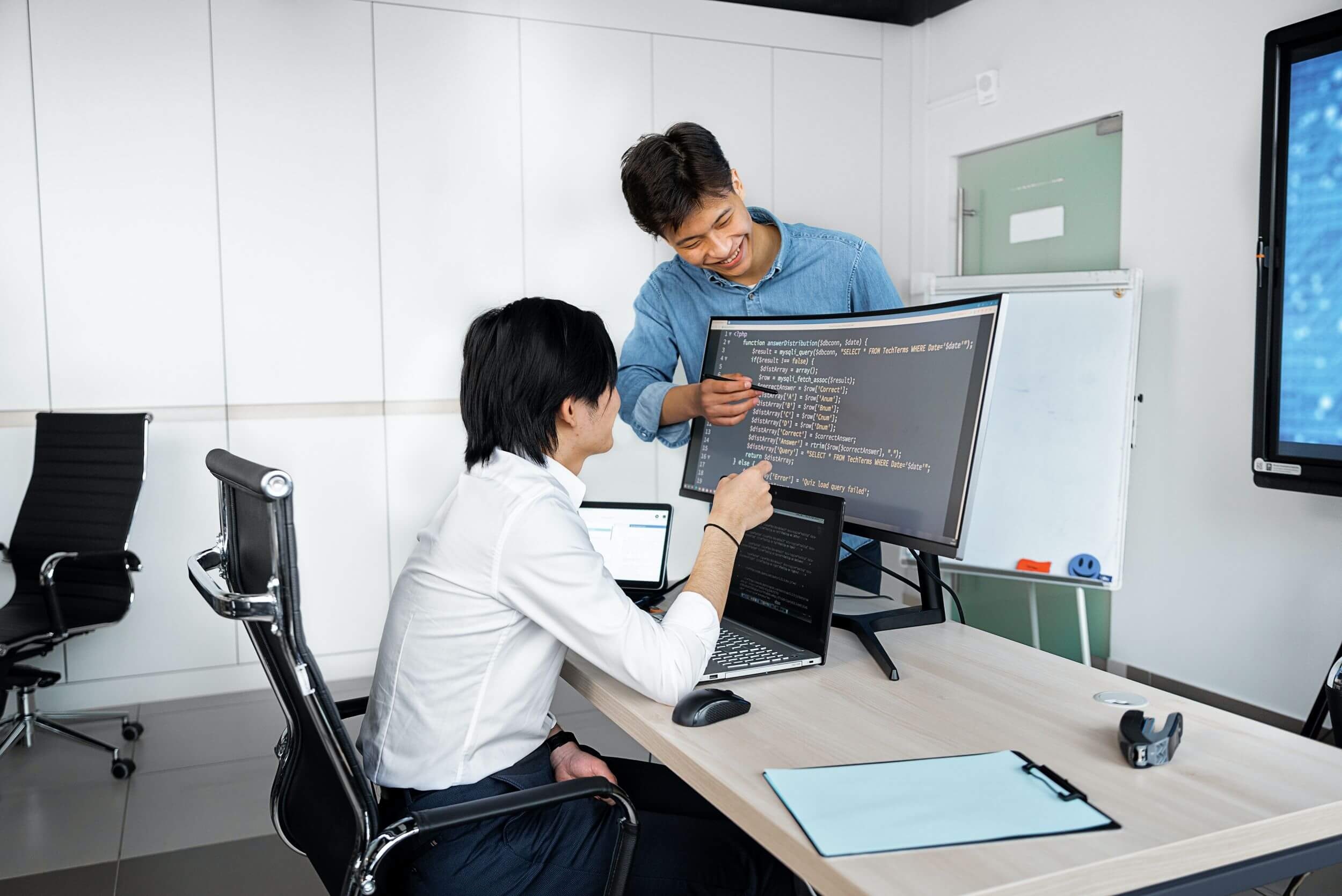 Two people evaluate code on computer monitor.