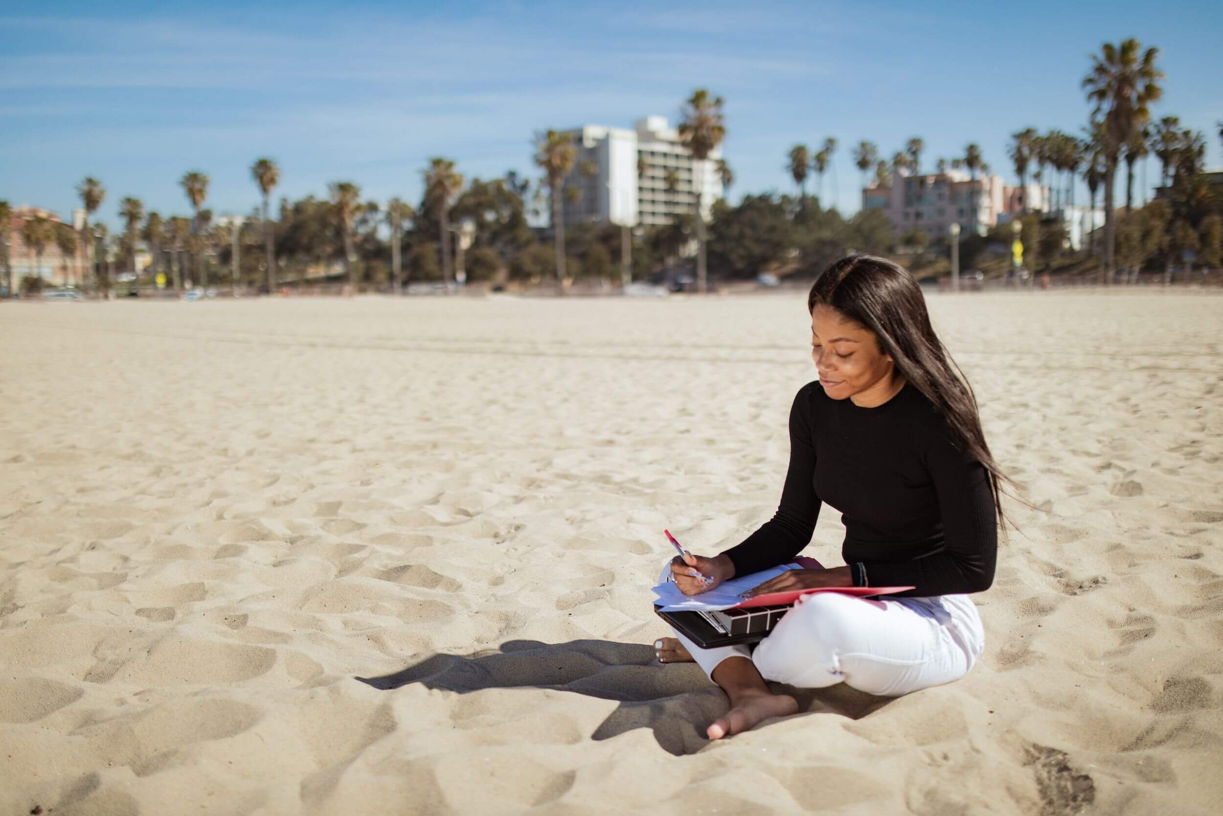 Person writing in folder, sitting on a beach.
