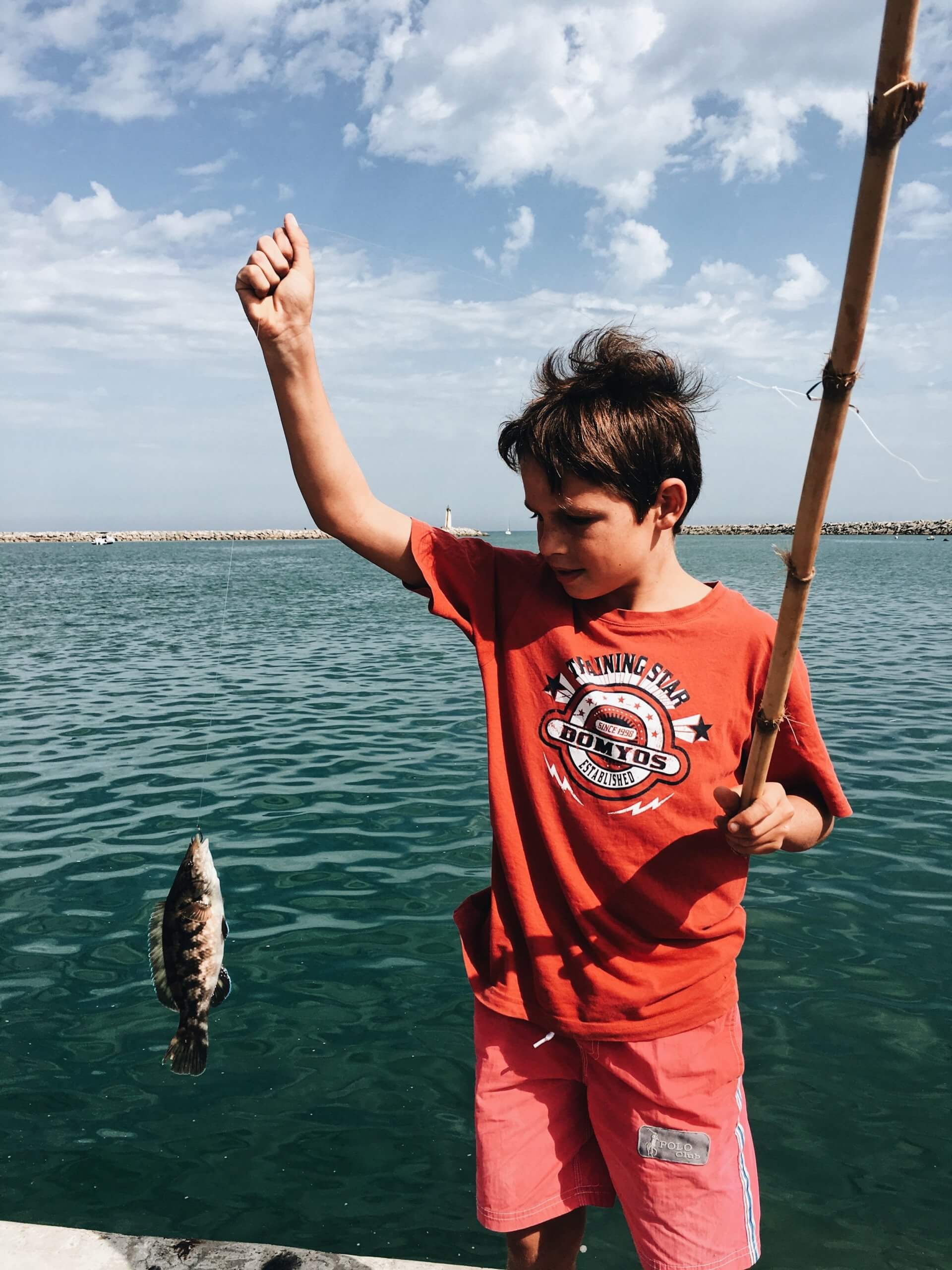 Young boy holds up caught fish.