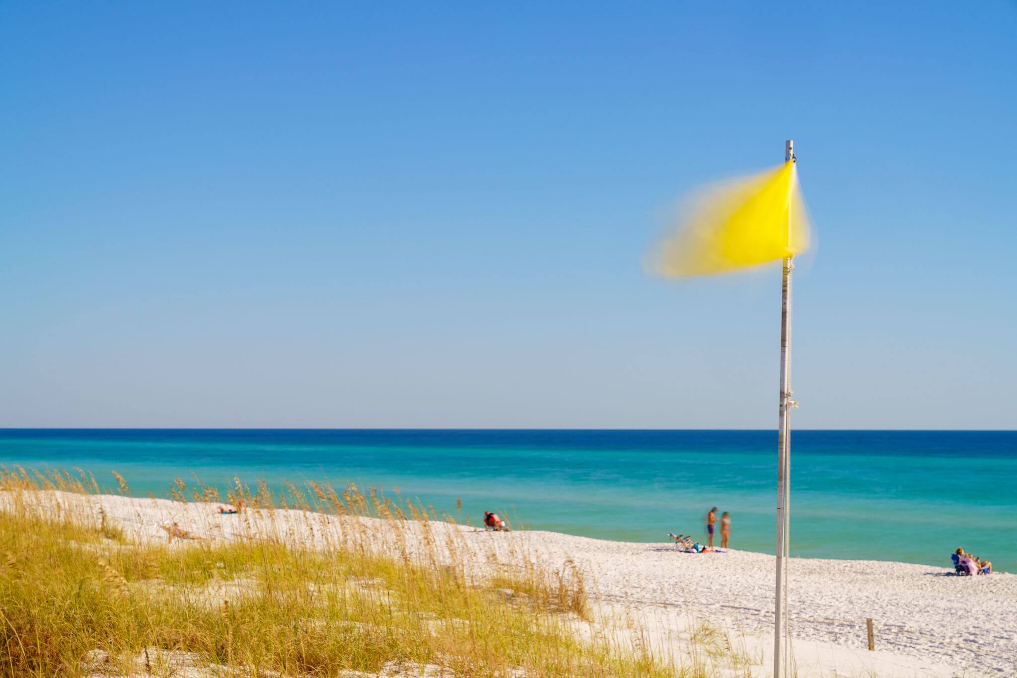 Yellow flag on scarsely filled white-sand beach.