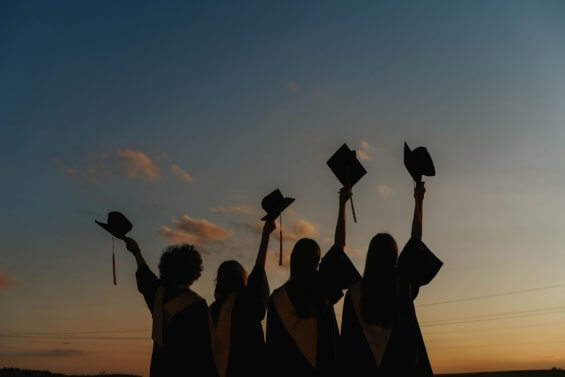 A silouhette of four graduates holding up their caps in the air.